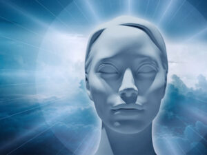 An all white female head with hair pulled back and eyes serenely closed. There is soft blue and white clouds behind her head and soft white rays of light emitting from her head.