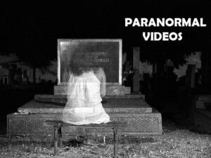 A dark night with a bench in front of a gravestone. A see through female ghost sits on the bench with her back to us looking at the gravestone.