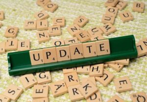 Scrabble letter tiles on a table with a light gold tablecloth. A green letter stand reads Update.