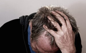 A man with his head bent, hand on the head in a position of despair or frustration