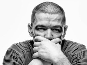 Black and white photo of man with hands crossed over his mouth as to not speak.