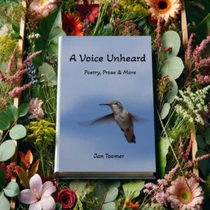 A book lies on a bed of flowers and greenery. The blue cover has a picture of a hummingbird. The cover reads A Voice Unheard: Poetry, Prose & More. Jan Toomer